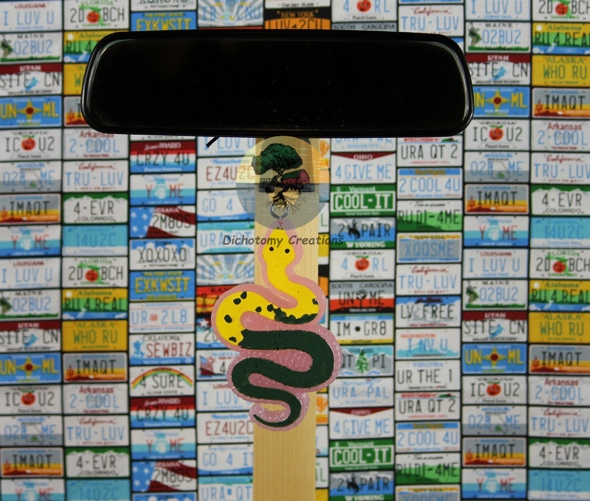 A pink freshie featuring a yellow and green coiled snake, set against a background of colorful license plates.