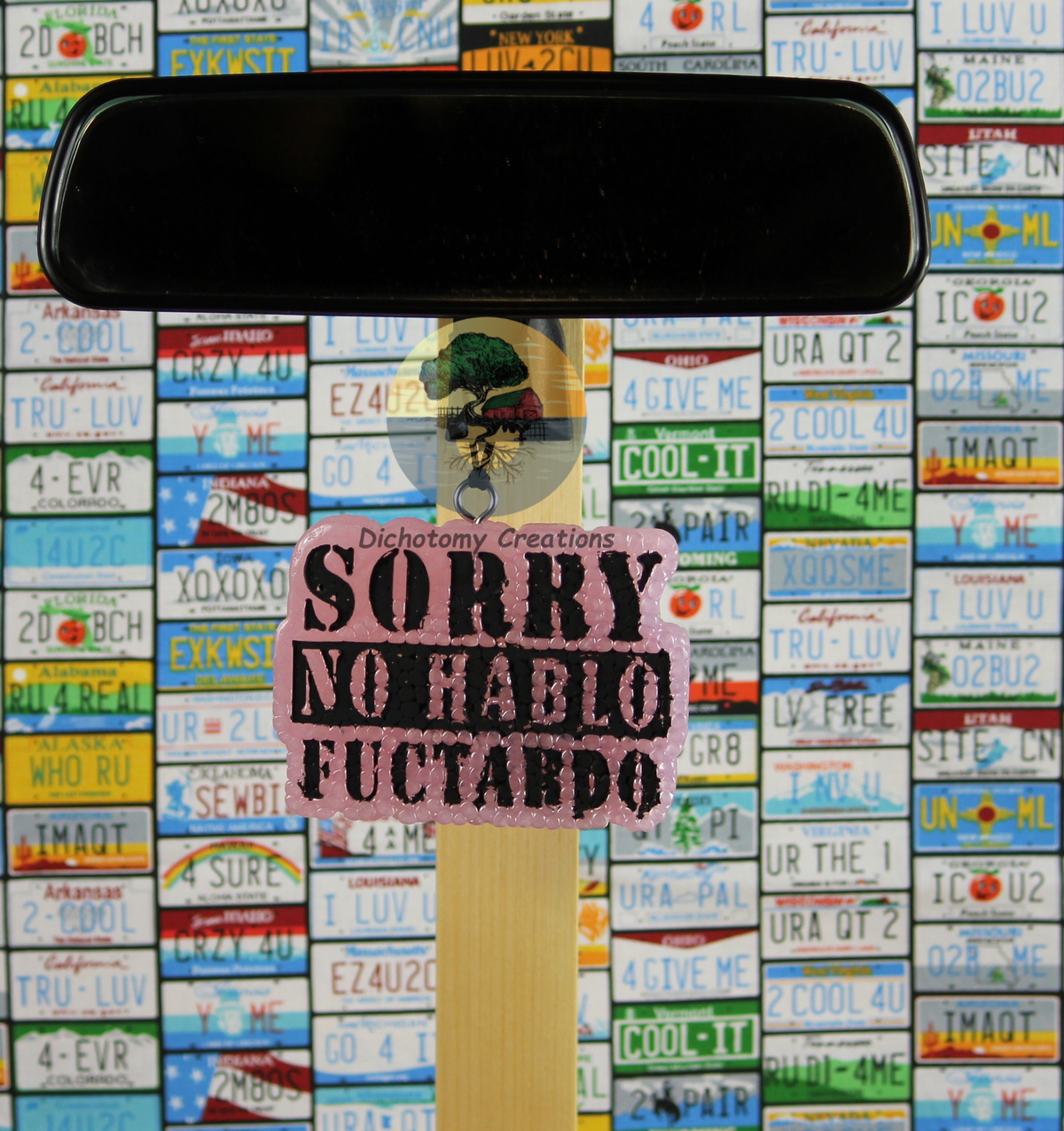 A pink freshie with the words "Sorry No Hablo Fuctardo". Displayed from a rearview mirror with a background of colorful license plates.