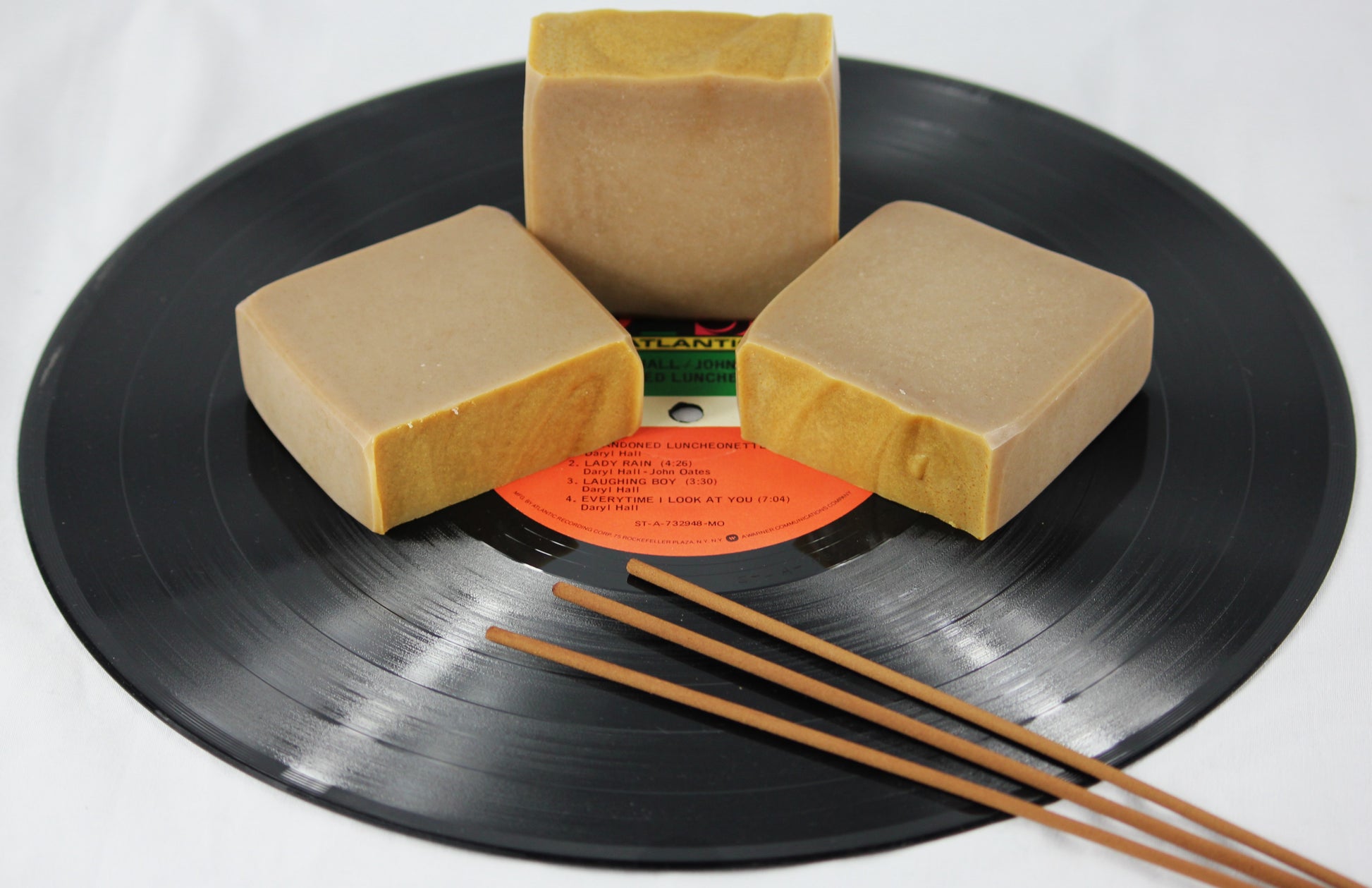 three bars of patchouli scented soap on a vinyl record, accented with incense sticks.