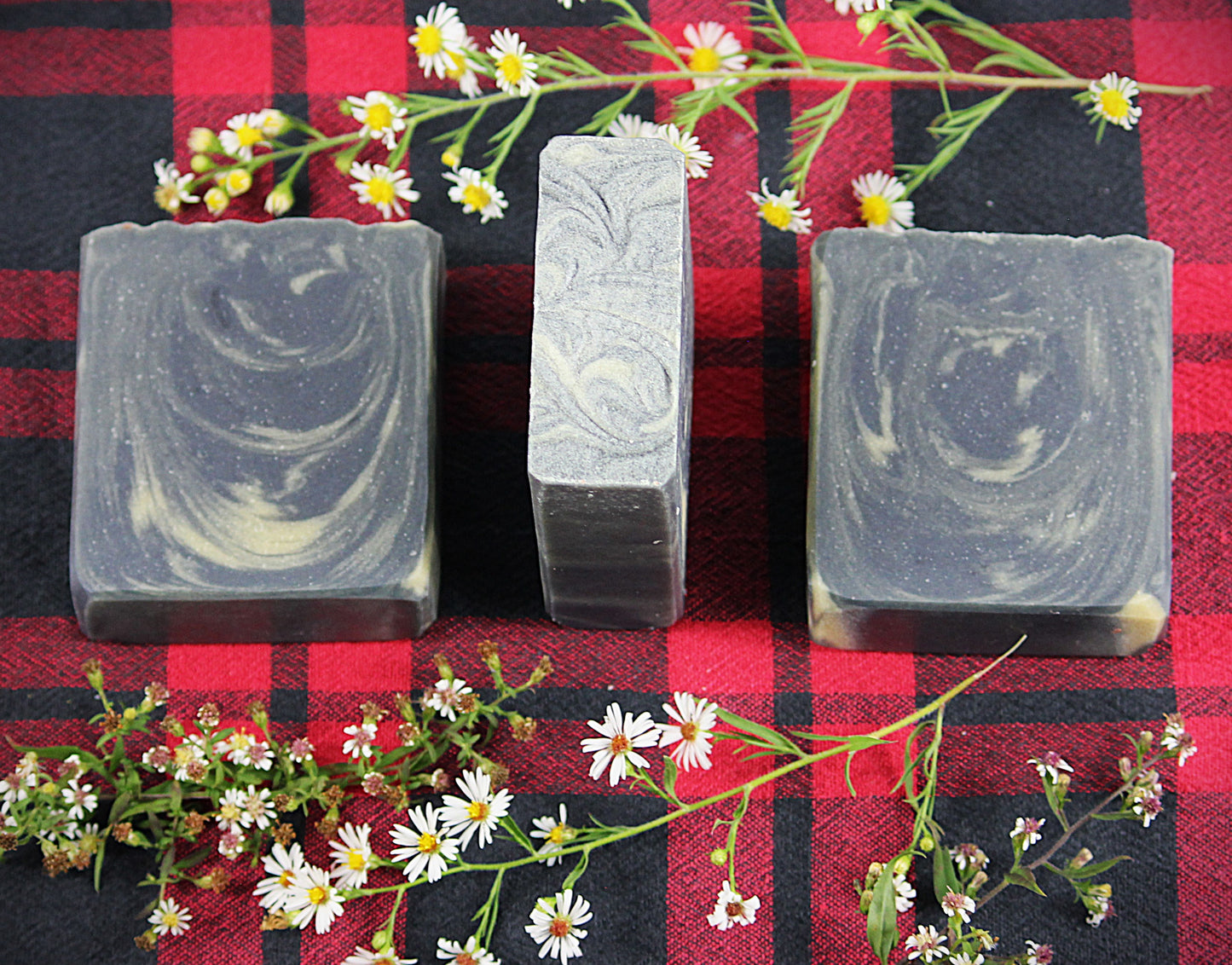 black with yellow swirls soap bars on a red and black plaid background, encircled by chamomile flowers