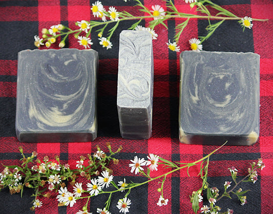 black with yellow swirls soap bars on a red and black plaid background, encircled by chamomile flowers