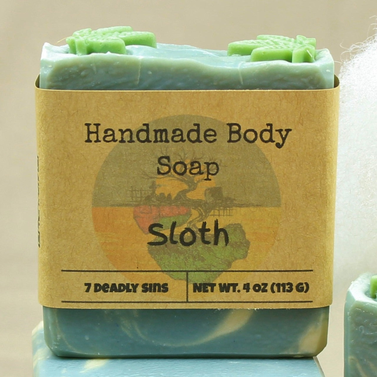 Pictured handmade body soap bar, Sloth.  Shown with label.  Soap is sky blue and white, with green cannabis leaf shaped soap on top, and scented in cannabis flower.