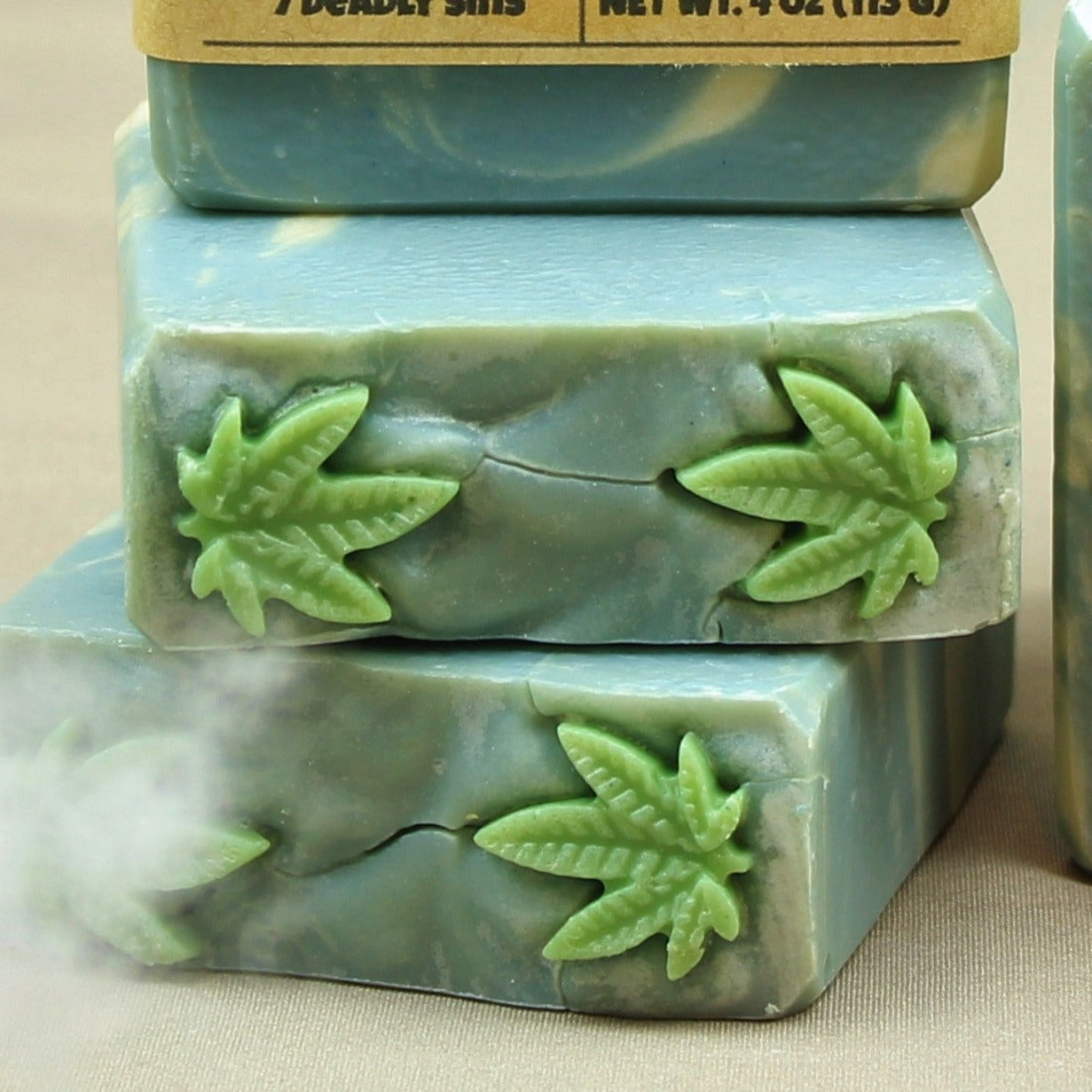Pictured handmade body soap bar, Sloth. Top of soap bars are shown, with small, green cannabis leaf soap embeds.
