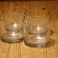 Four clear glass tumblers arranged on a light brown wooden tabletop.