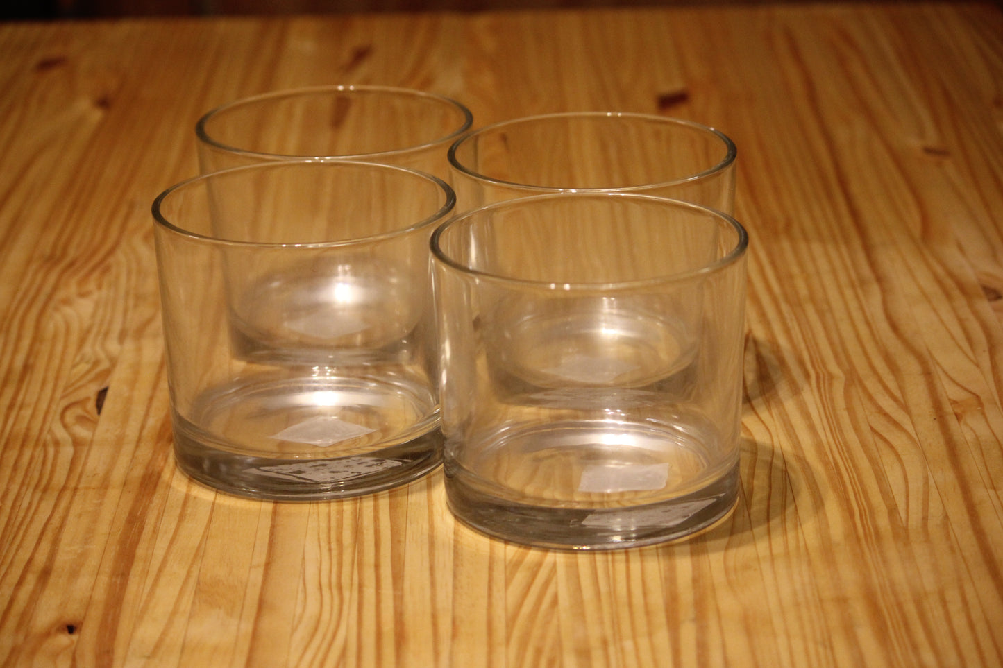 Four clear glass tumblers arranged on a light brown wooden tabletop.