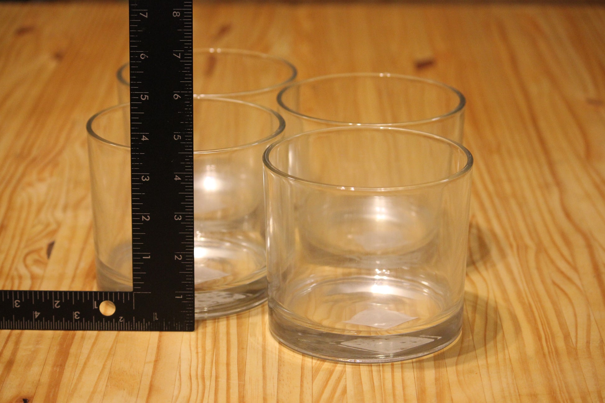 Three clear glass tumblers on a light wood surface next to a black ruler for scale.