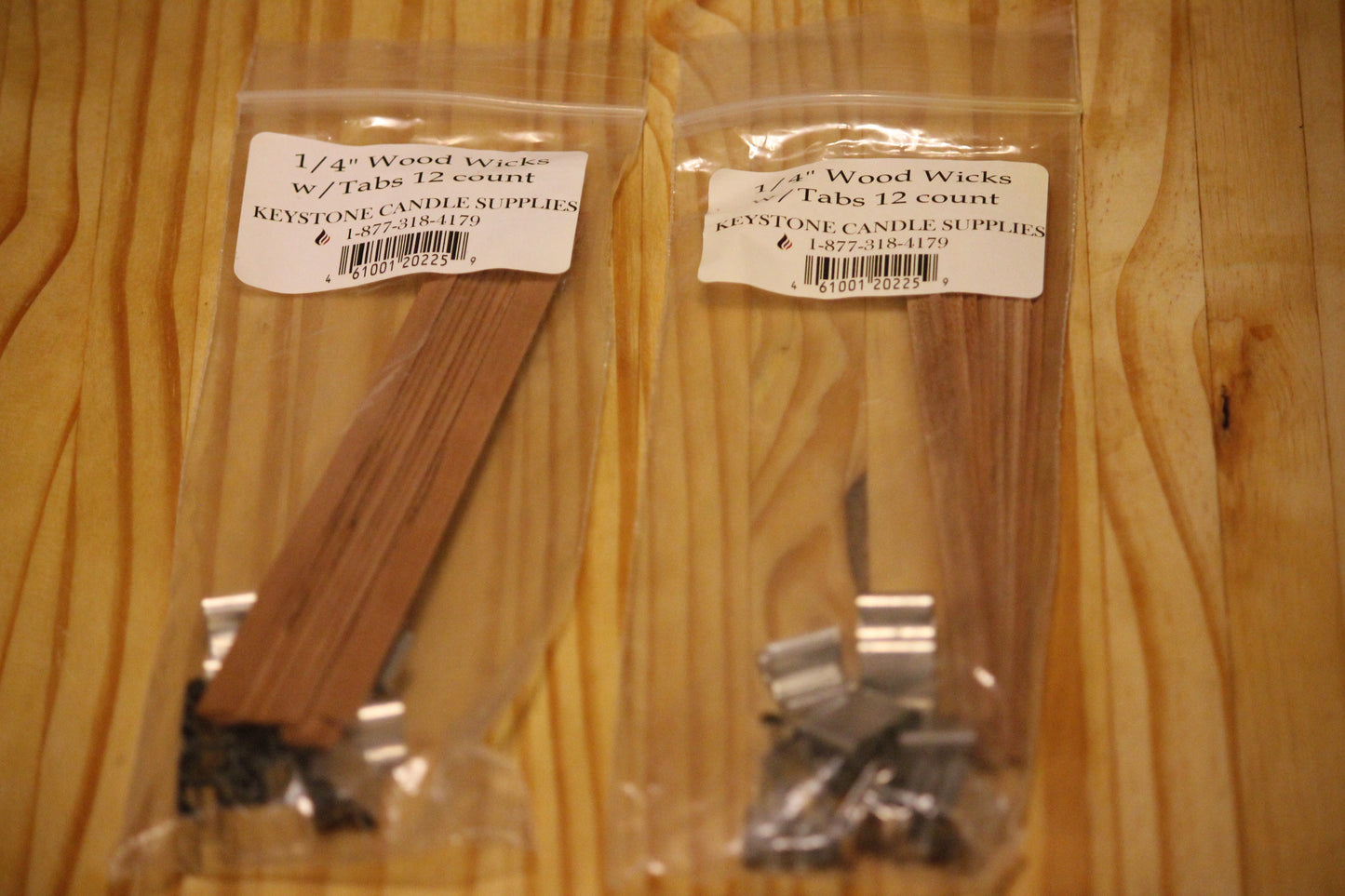 Two clear plastic bags of Keystone Candle Supply 1/4 inch wood wicks with tabs, 12 count each, placed on a light wood grain surface. 