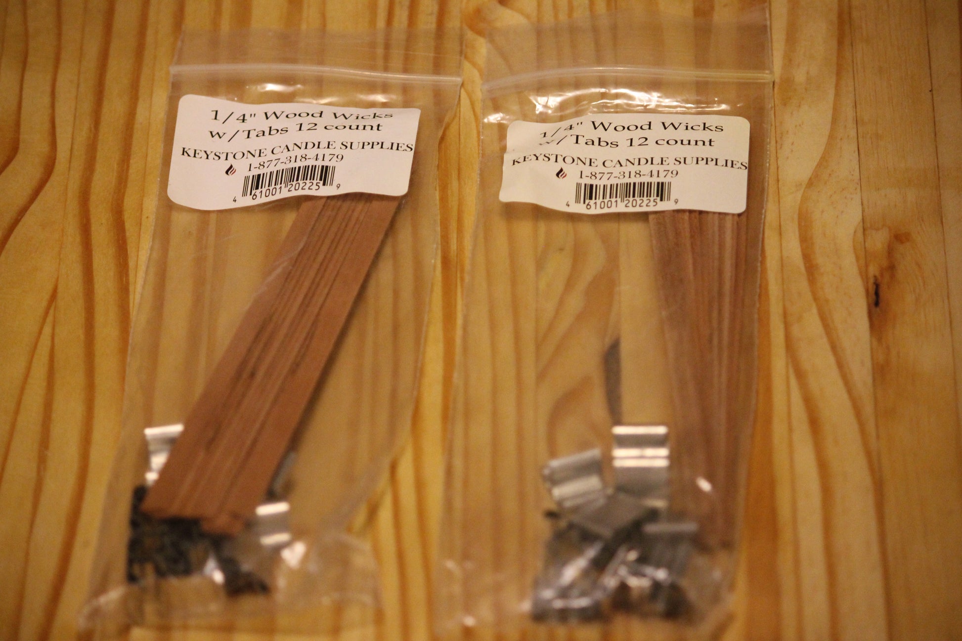 Two clear plastic bags of Keystone Candle Supply 1/4 inch wood wicks with tabs, 12 count each, placed on a light wood grain surface. 
