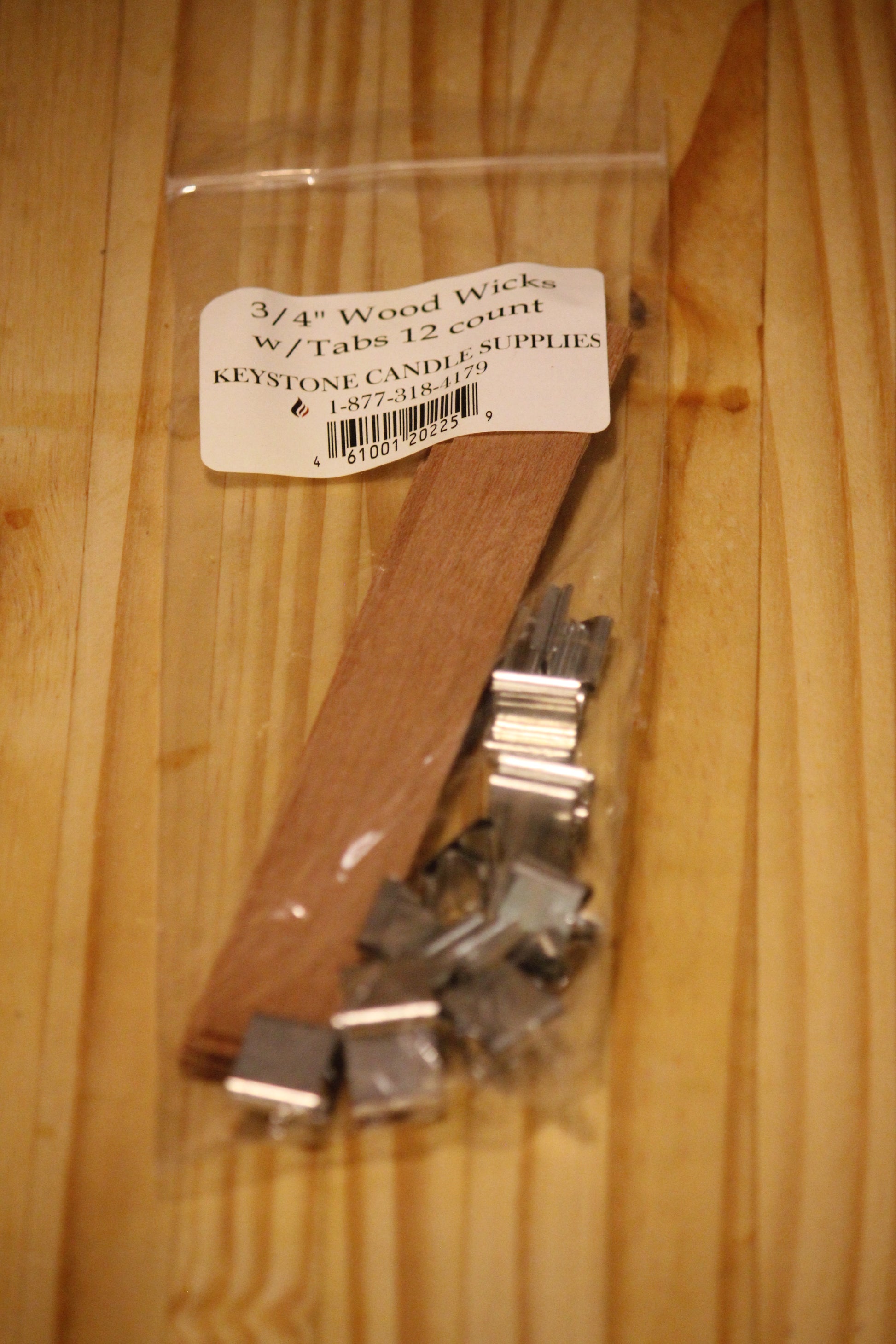 A clear plastic bag containing 3/4 inch wood wicks with metal tabs, labeled 'Keystone Candle Supplies', placed on a light wood grain surface.