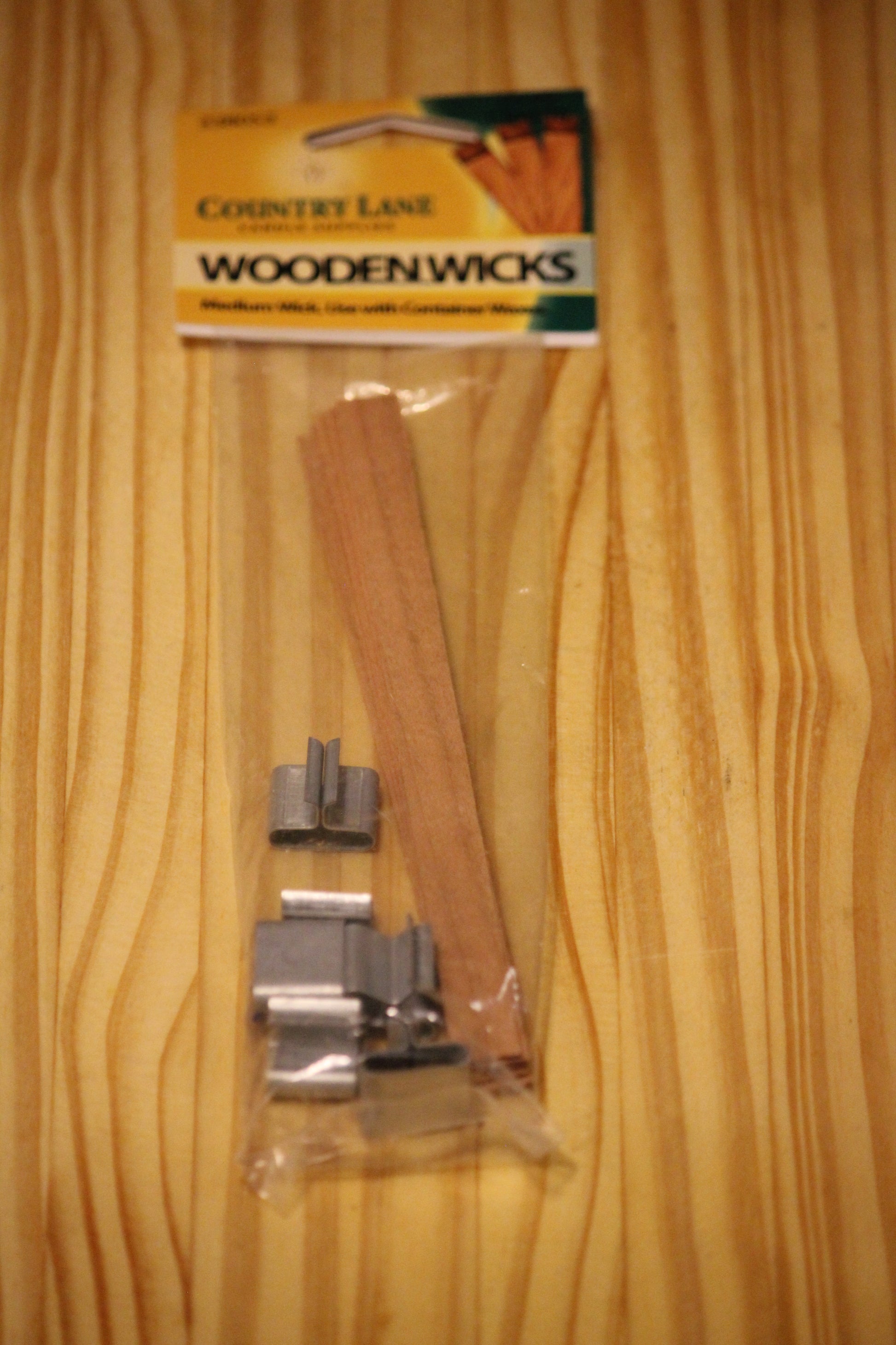 A package of Country Lane Wooden Wicks containing  wooden wicks and silver metal wick clips, displayed on a light wood grain surface.