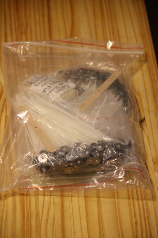 A clear plastic zip-top bag containing various wicks and wick supplies, placed on a light wood-grained tabletop.