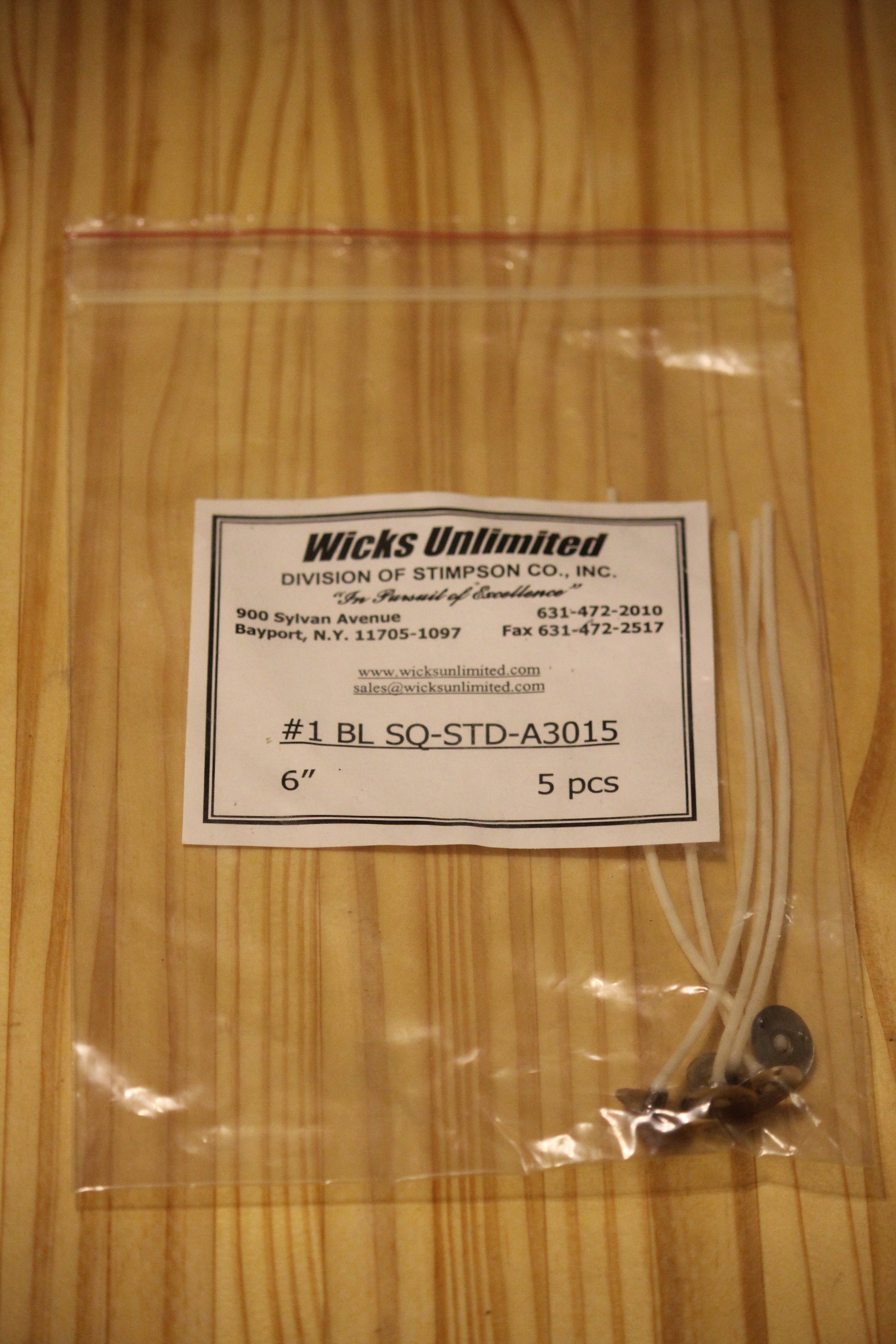 A clear plastic zip-top bag containing five six inch pre-tabbed wicks, with a white paper label reading 'Wicks Unlimited' and product code '#1 BL SO-STD-A3015 6" 5 pcs' placed on a light wood surface.