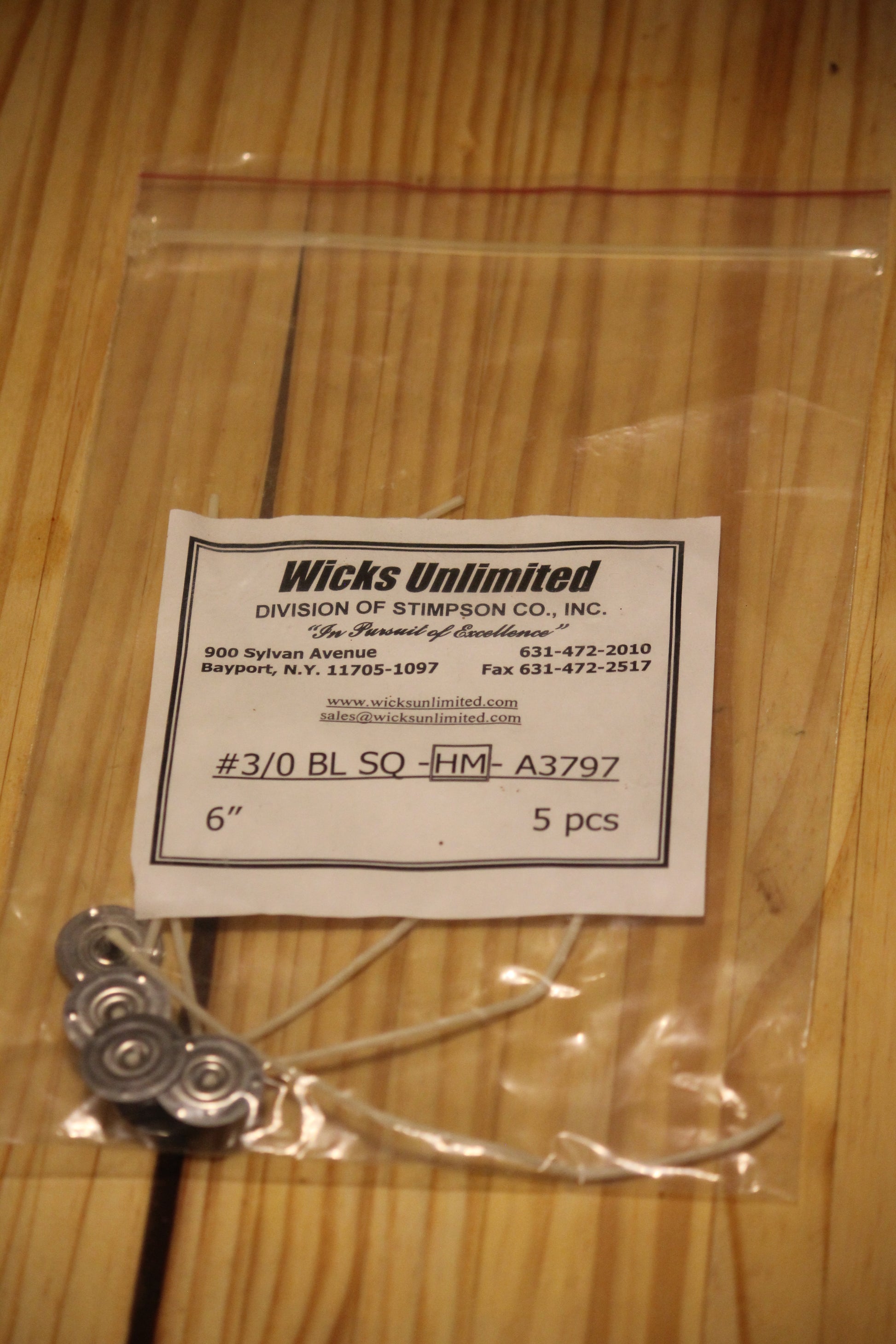 A clear plastic zip-top bag containing five six inch pre-tabbed wicks, with a white paper label from Wicks Unlimited, placed on a light wood surface.