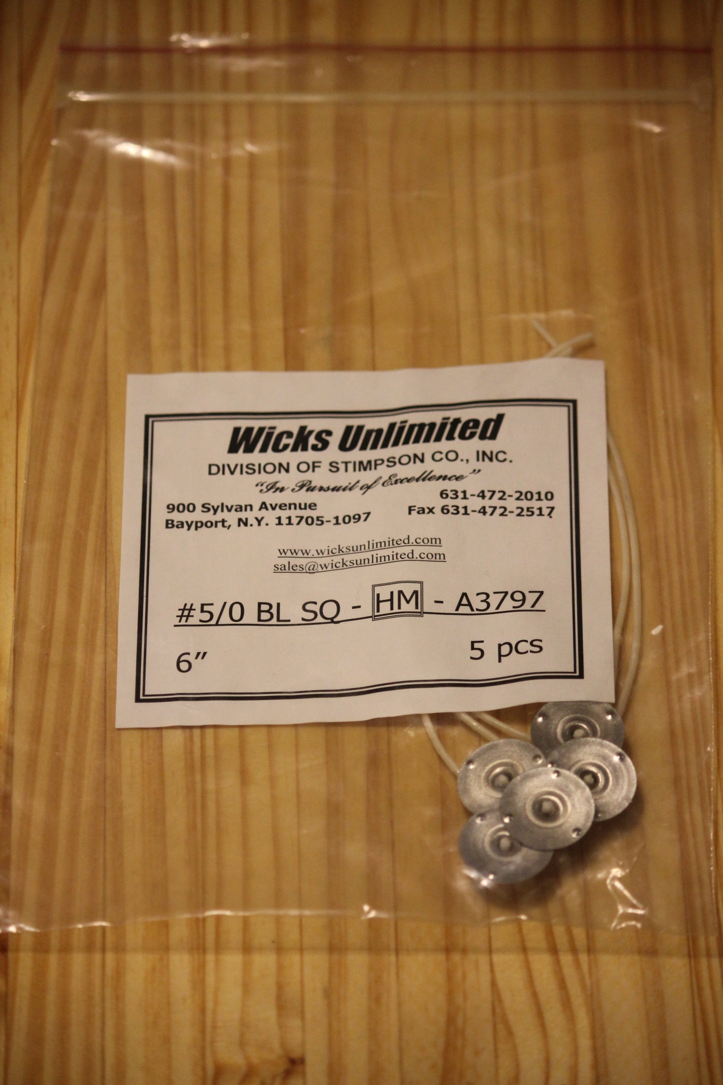 A clear plastic zip-top bag containing five six inch pre-tabbed wicks next to a white paper label that reads 'Wicks Unlimited' and shows product details, placed on a light wood surface.