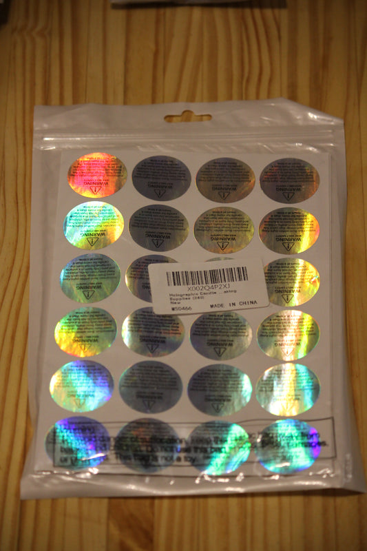 A clear plastic bag containing a sheet of round holographic wax melt warning stickers on a wooden surface. 