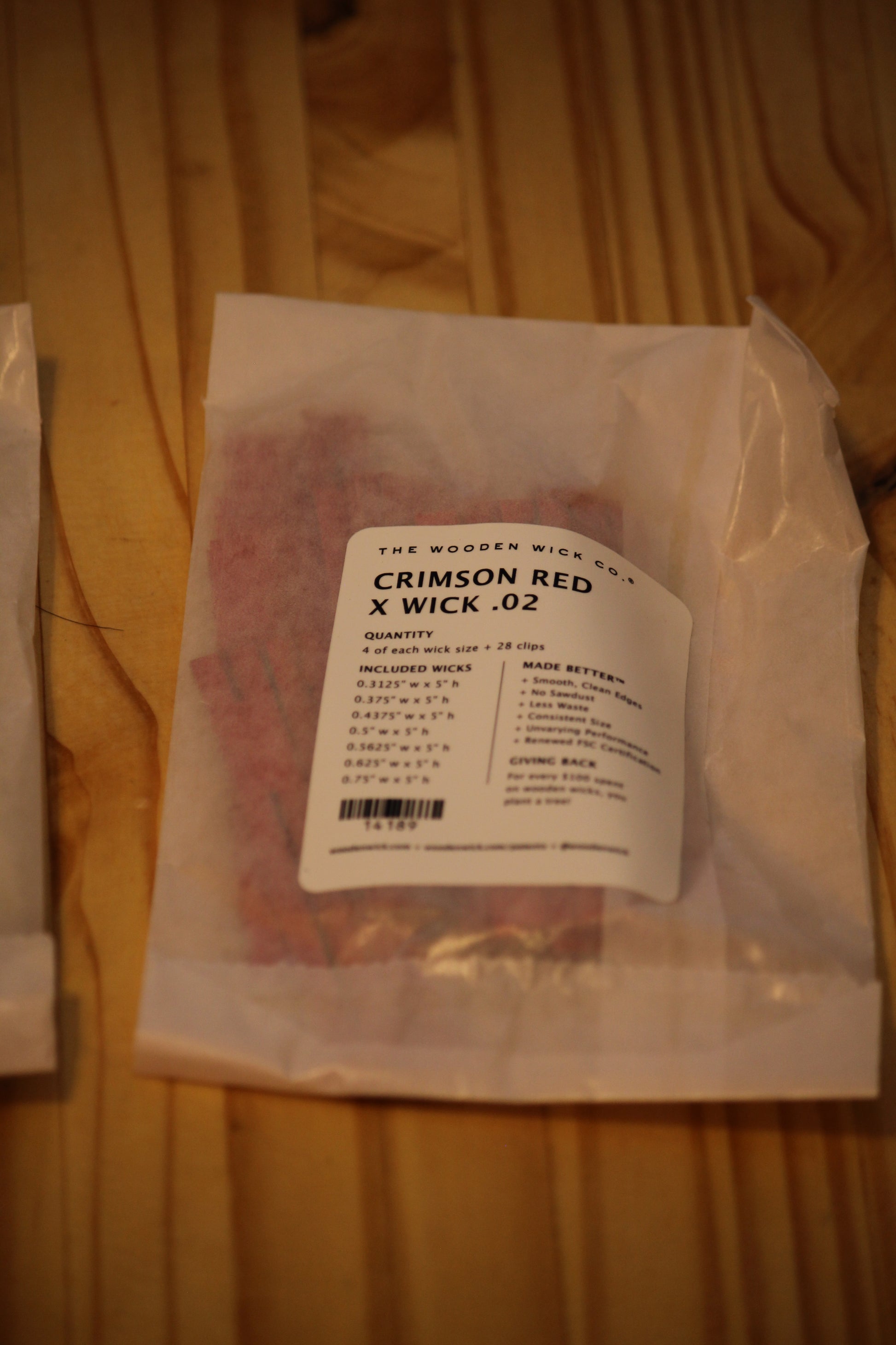 A clear plastic bag containing red wood wicks, with a white label reading 'THE WOODEN WICK CO. CRIMSON RED X WICK .