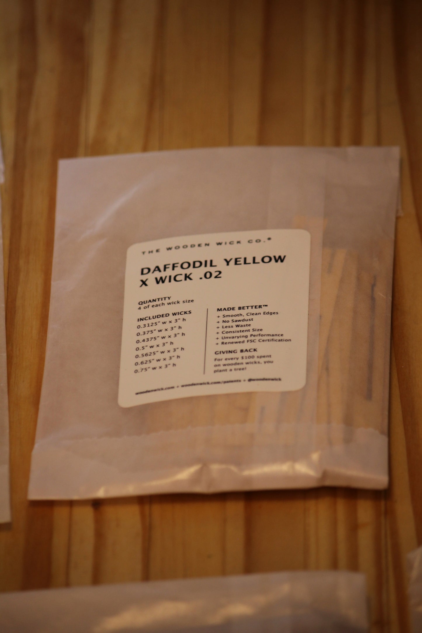 A clear plastic bag containing wood wicks, featuring a white label that reads 'DAFFODIL YELLOW X WICK .02' from 'The Wooden Wick Co.