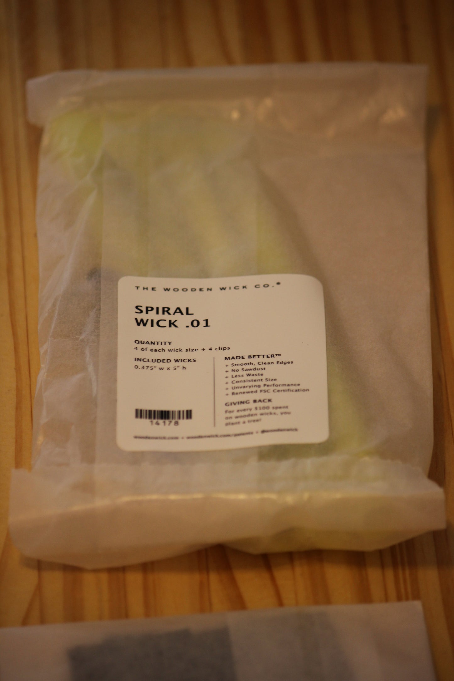 A packaged bundle of spiral wicks from The Wooden Wick Co. in a clear plastic bag with a white label, resting on a wooden surface.
