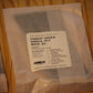 A packaged bundle of WICK .02 single-ply wood wicks in forest green, sealed in a clear plastic bag with a white label, resting on a light wood surface.
