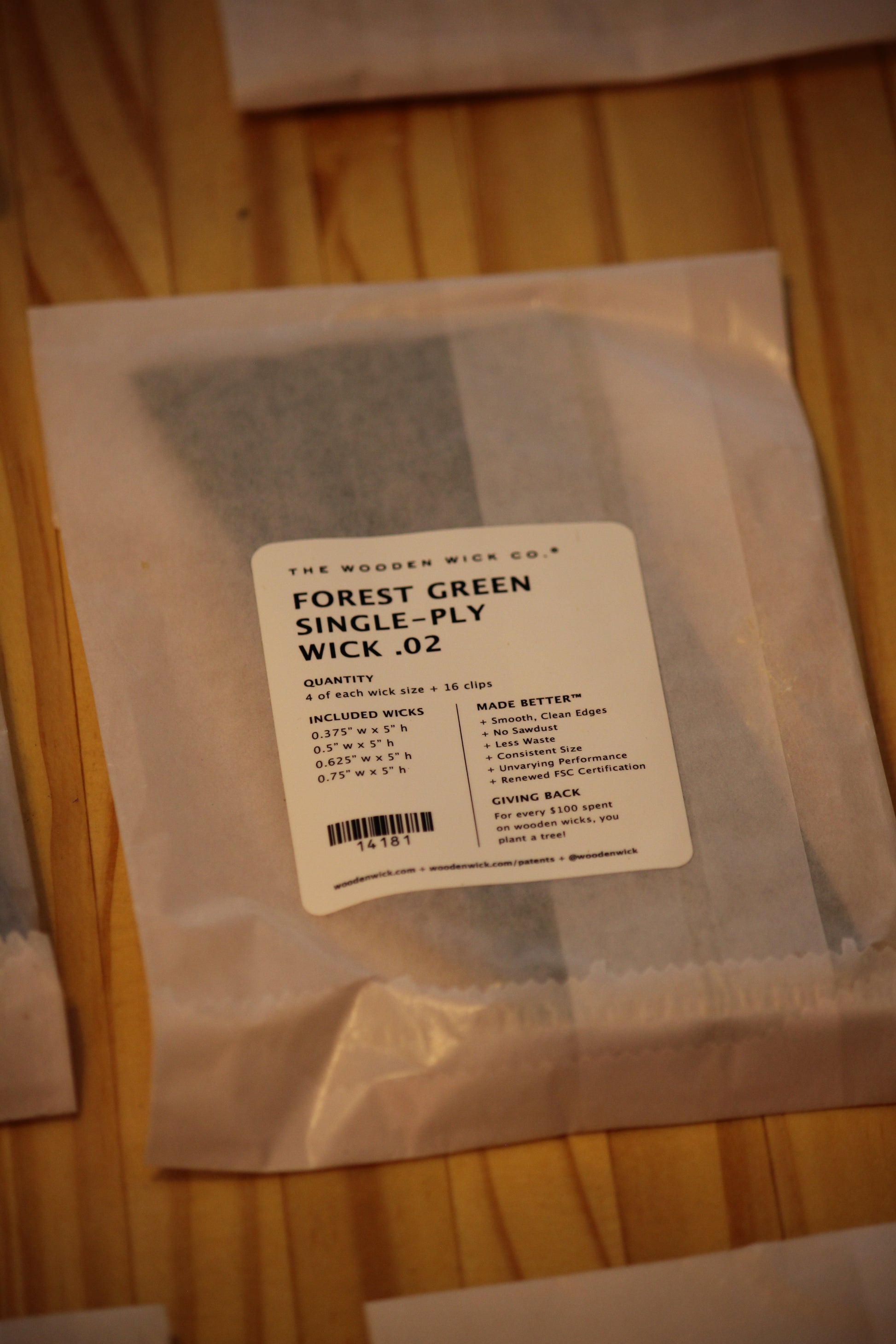 A packaged bundle of WICK .02 single-ply wood wicks in forest green, sealed in a clear plastic bag with a white label, resting on a light wood surface.