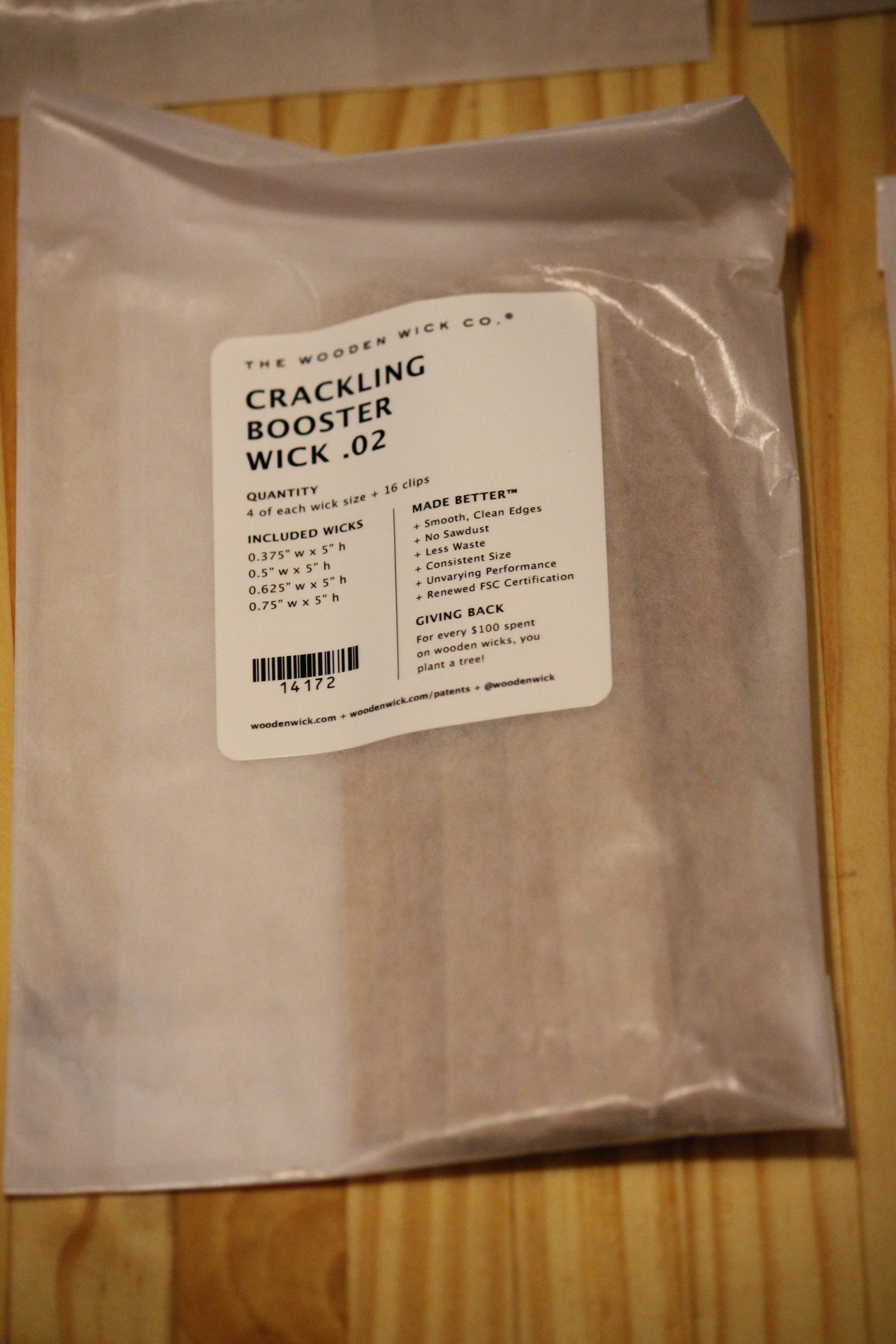A sealed clear plastic pouch containing wood wicks, with a white label reading 'Crackling Booster Wick .02' from The Wooden Wick Co.