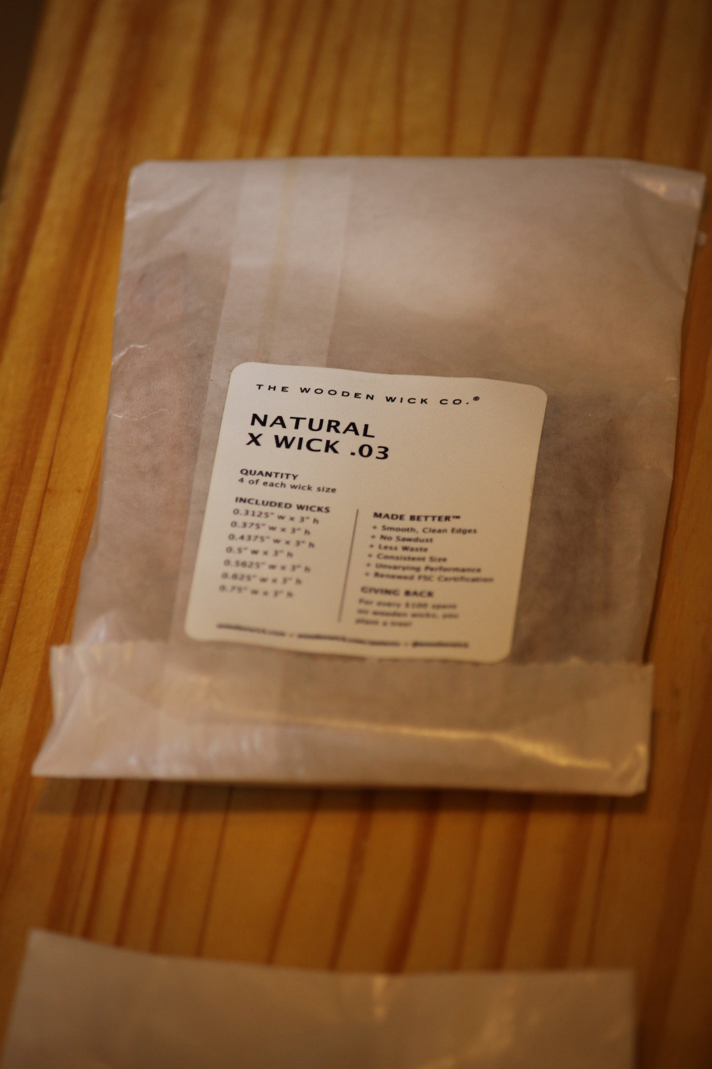 A clear plastic bag containing natural wood wick material, with a white label reading 'THE WOODEN WICK CO. NATURAL X WICK .