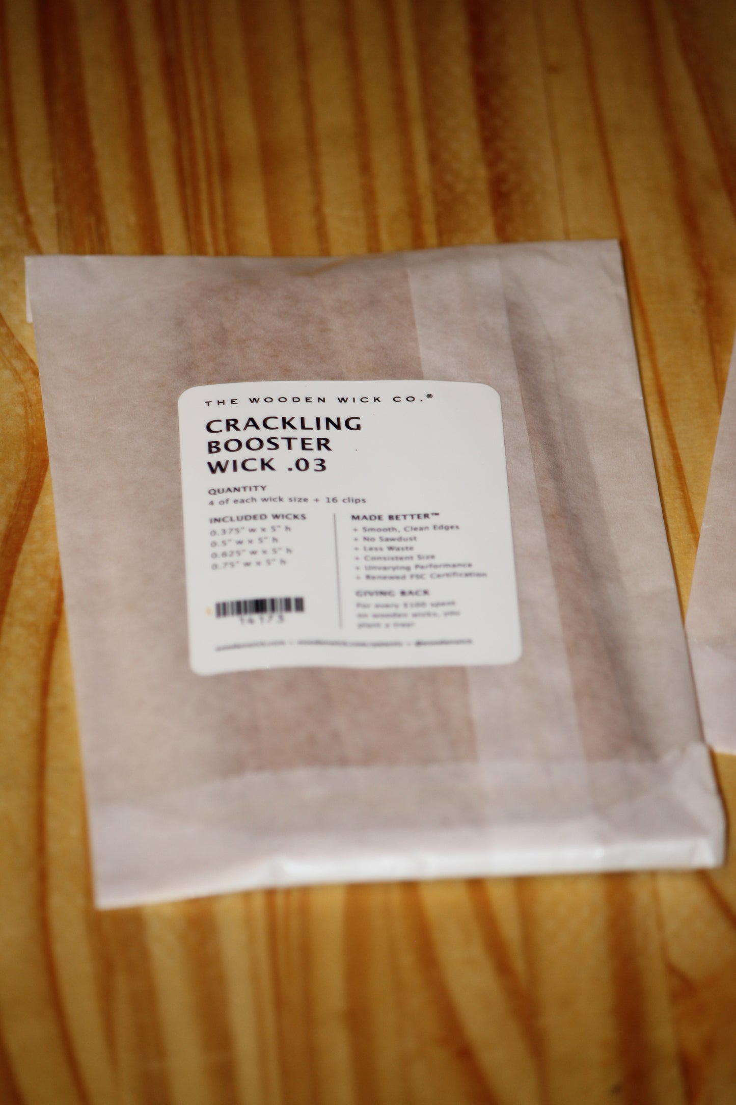 A sealed paper packet labeled 'The Wooden Wick Co. Crackling Booster Wick .03' placed on a light wood surface.