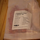 A clear plastic bag containing red wood wicks, with a white paper label reading 'THE WOODEN WICK CO. CRIMSON RED X WICK .