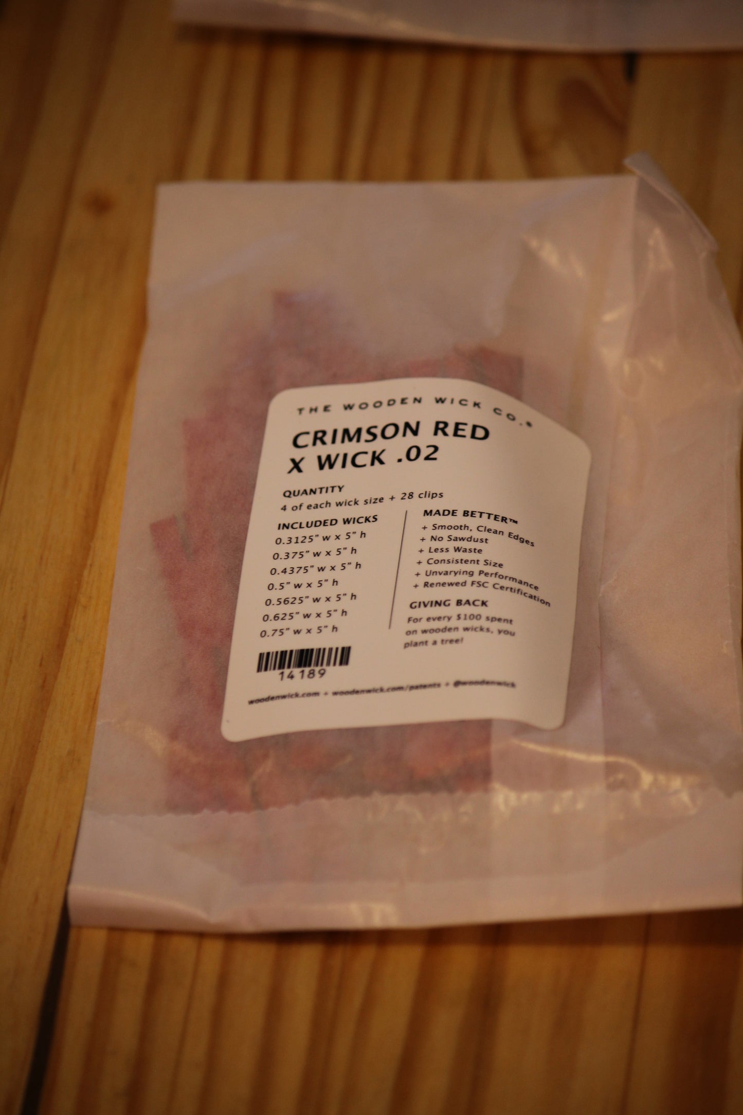 A clear plastic bag containing red wood wicks, with a white paper label reading 'THE WOODEN WICK CO. CRIMSON RED X WICK .