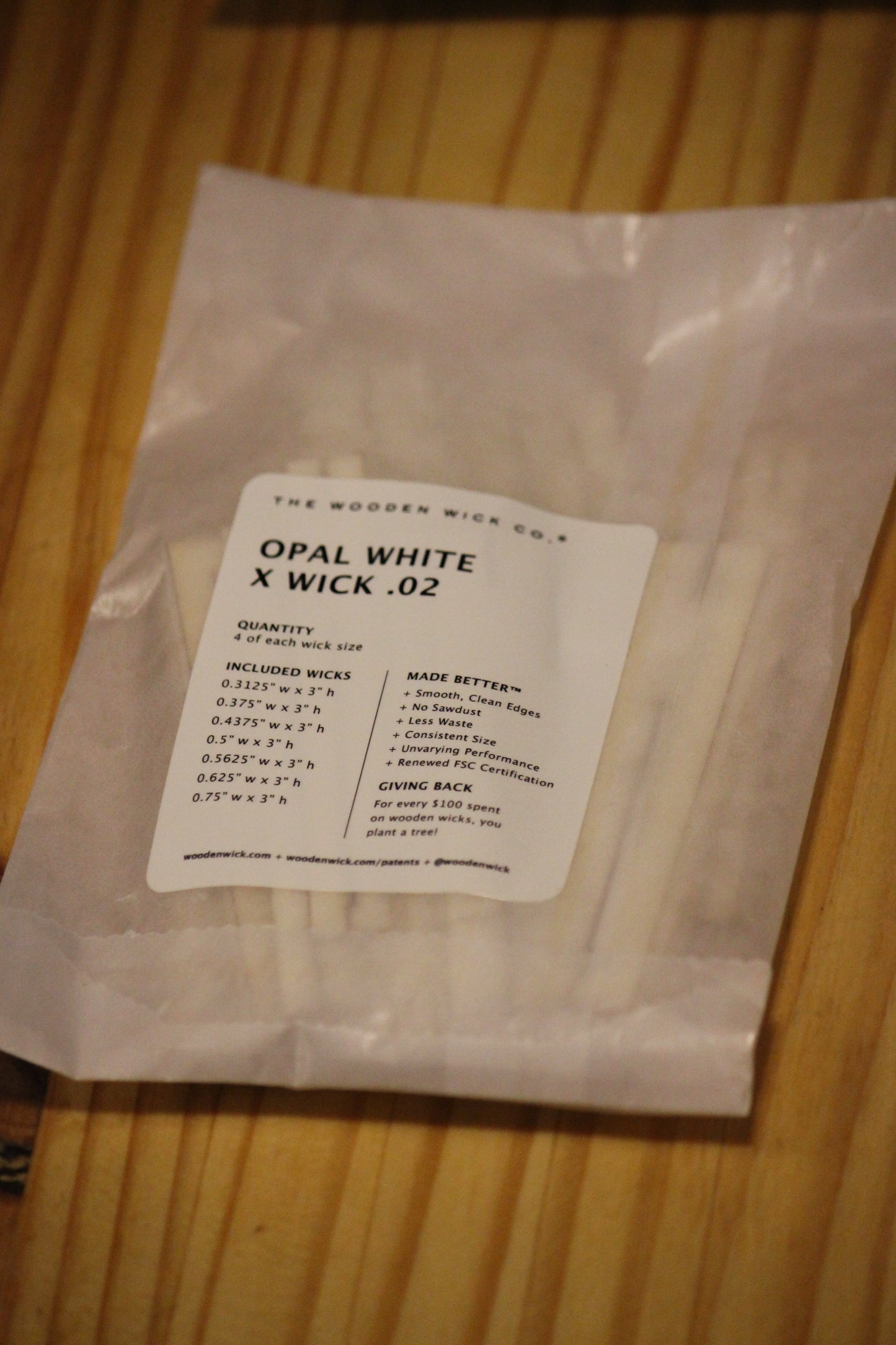 A clear plastic bag containing white wood wicks with a white paper label reading 'THE WOODEN WICK CO. OPAL WHITE X WICK .