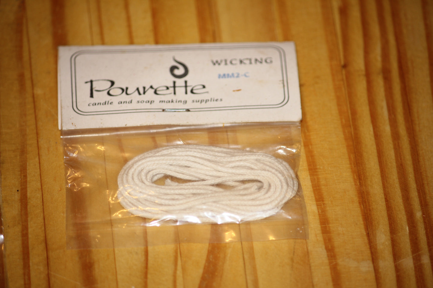 A package of white cotton wicking by Pourette, sealed in a clear plastic bag with a white paper header card, placed on a wooden surface.