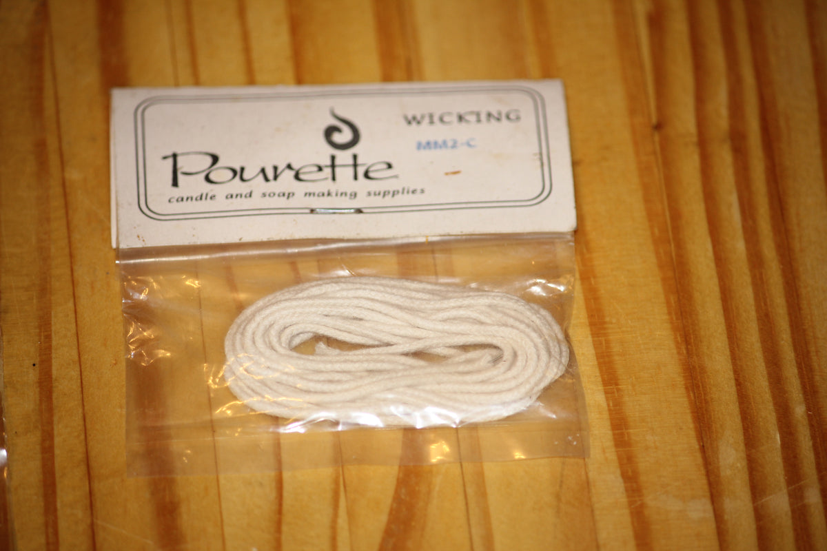 A package of white cotton wicking by Pourette, sealed in a clear plastic bag with a white paper header card, placed on a wooden surface.