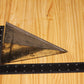 A triangular metal pillar mold, shown on a light wood grain background with a black L-square ruler and tape measure for scale.