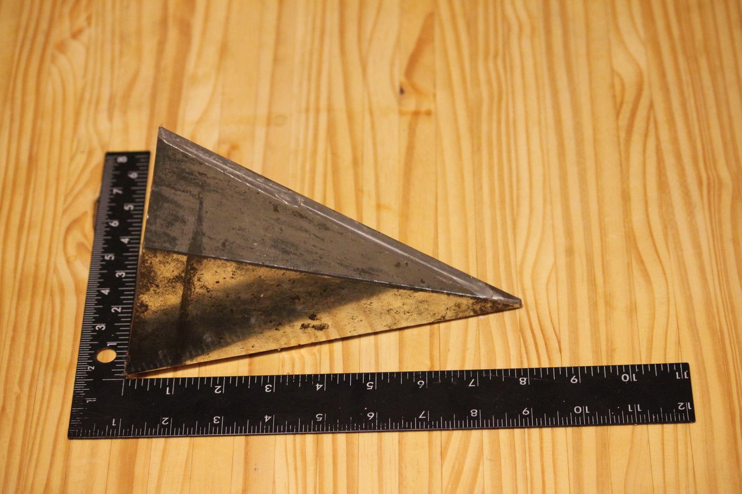 A triangular metal pillar mold, shown on a light wood grain background with a black L-square ruler and tape measure for scale.