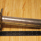 A used metal cylindrical pillar mold, shown on a light wood grain background with a black ruler for scale.