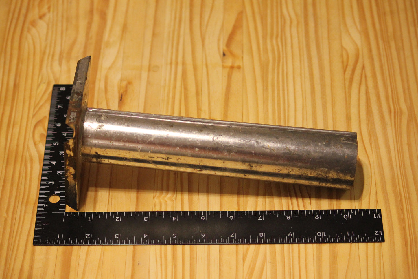 A used metal cylindrical pillar mold, shown on a light wood grain background with a black ruler for scale.