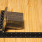 A metal square pillar mold, shown on a light wood grain background with a black ruler for scale.