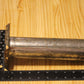 A metal cylindrical pillar mold, shown on a light wood grain background with a black ruler for scale.