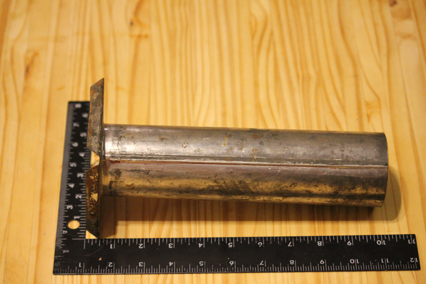 A metal cylindrical pillar mold, shown on a light wood grain background with a black ruler for scale.