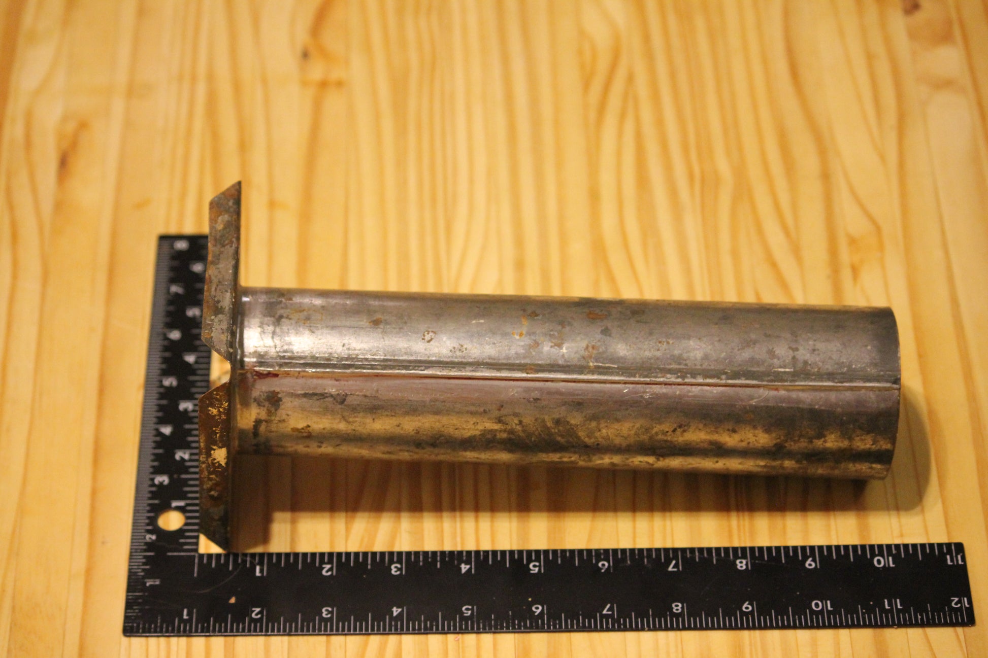A metal cylindrical pillar mold, shown on a light wood grain background with a black ruler for scale.