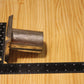 A metal cylindrical pillar mold, shown on a light wood grain background with a black ruler for scale.