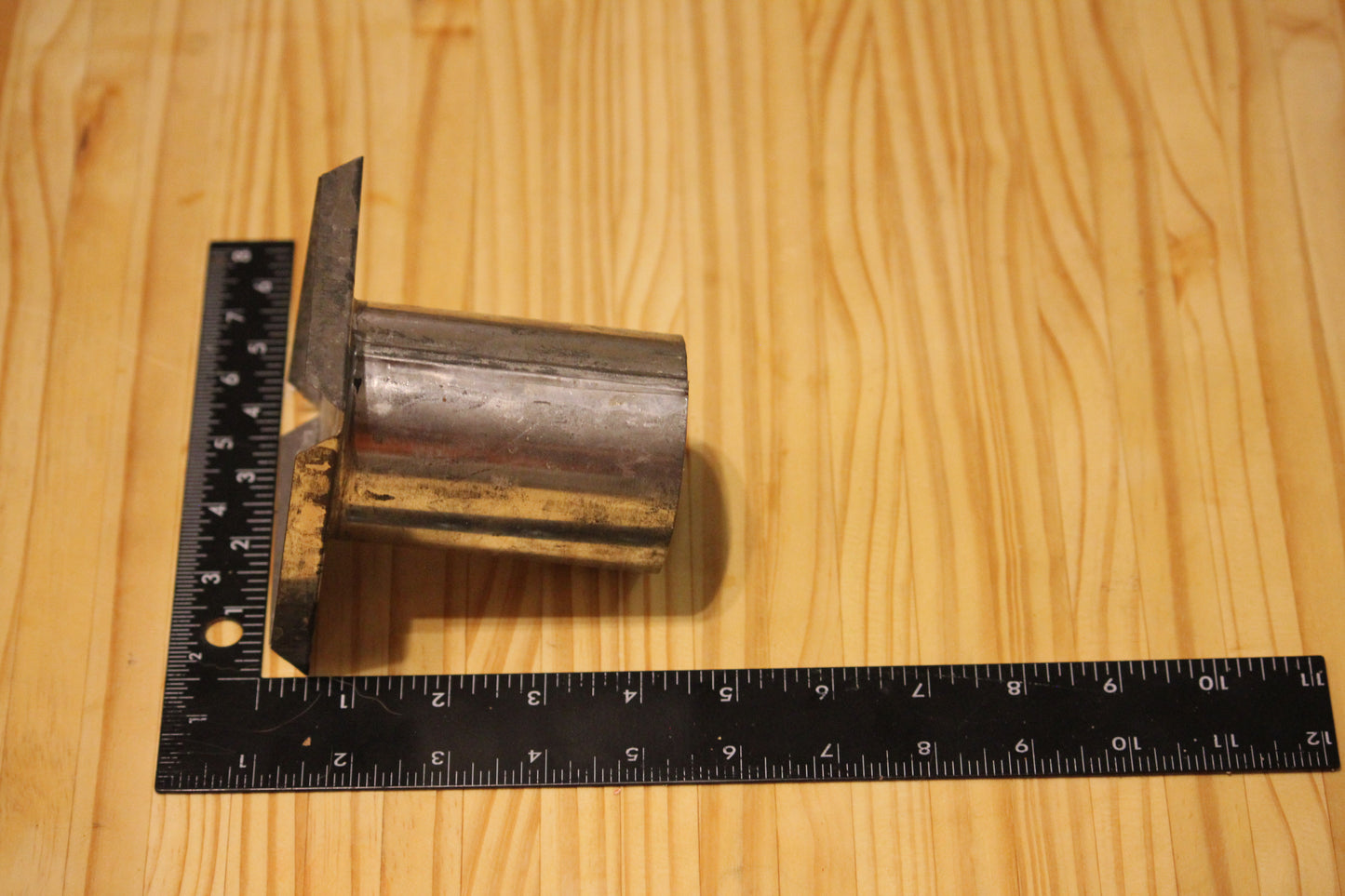 A metal cylindrical pillar mold, shown on a light wood grain background with a black ruler for scale.