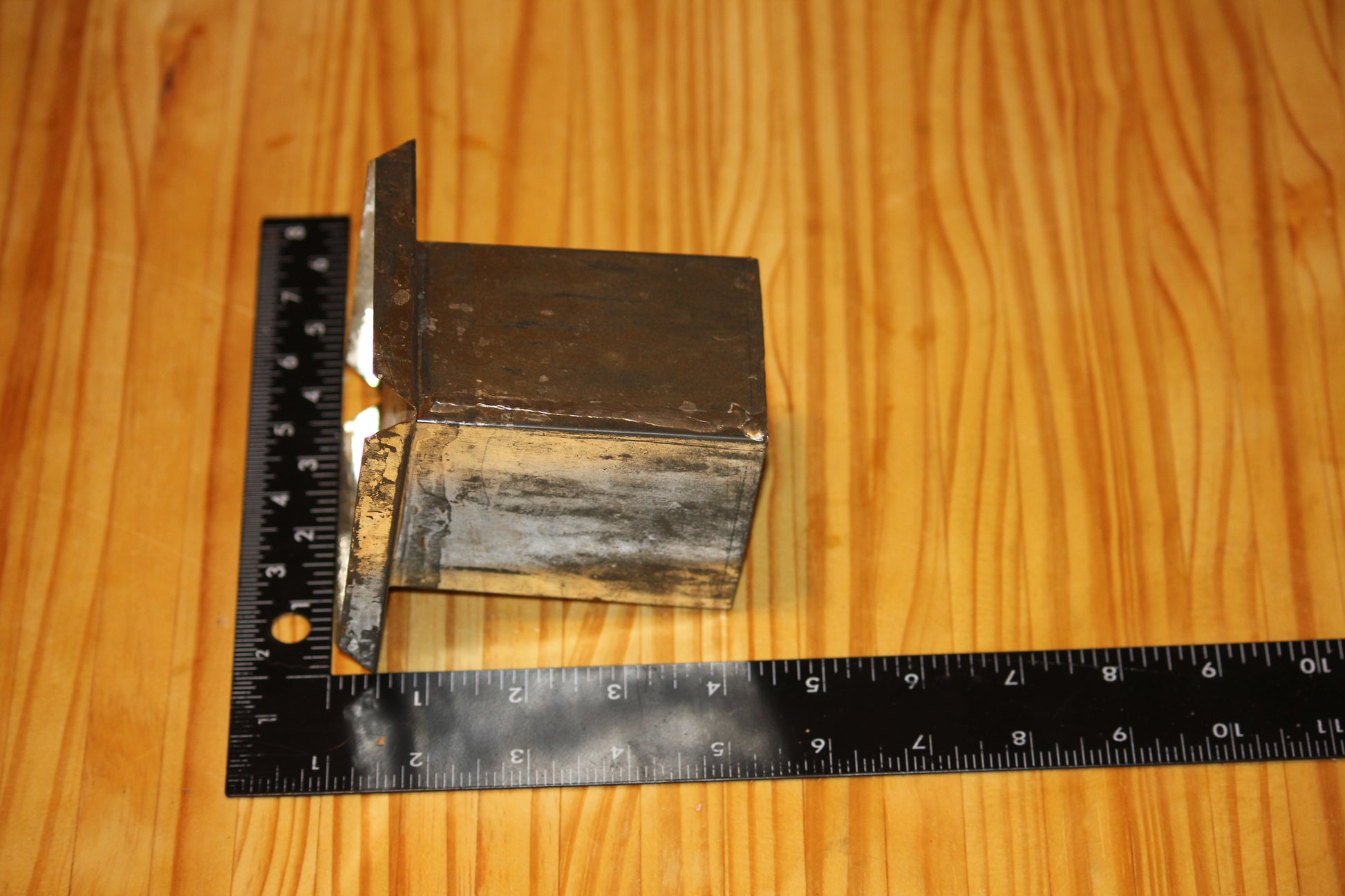 A metal square pillar mold, shown on a light wood grain background with a black ruler for scale.