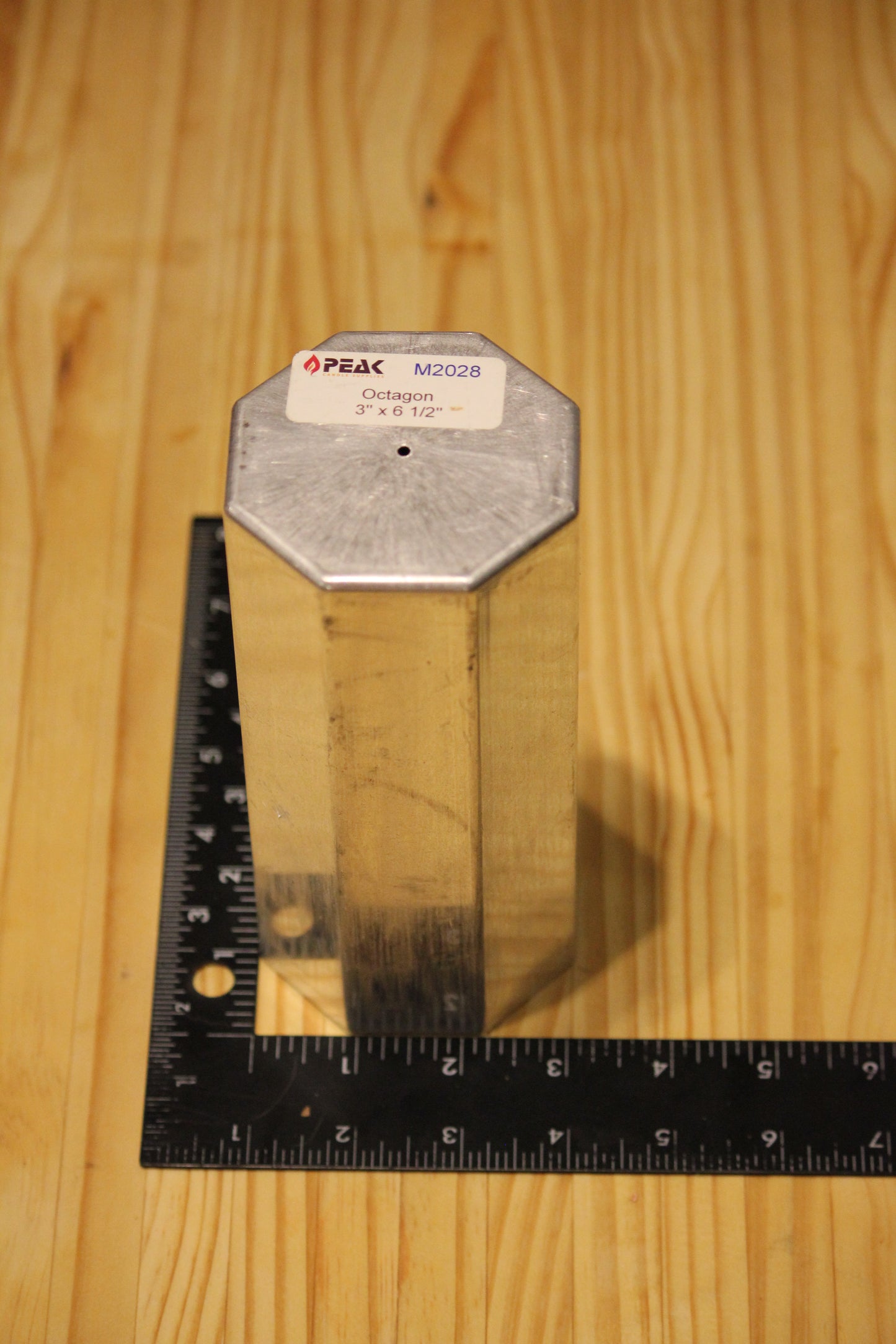 A metal octagon pillar mold, shown on a light wood grain background with a black ruler for scale.