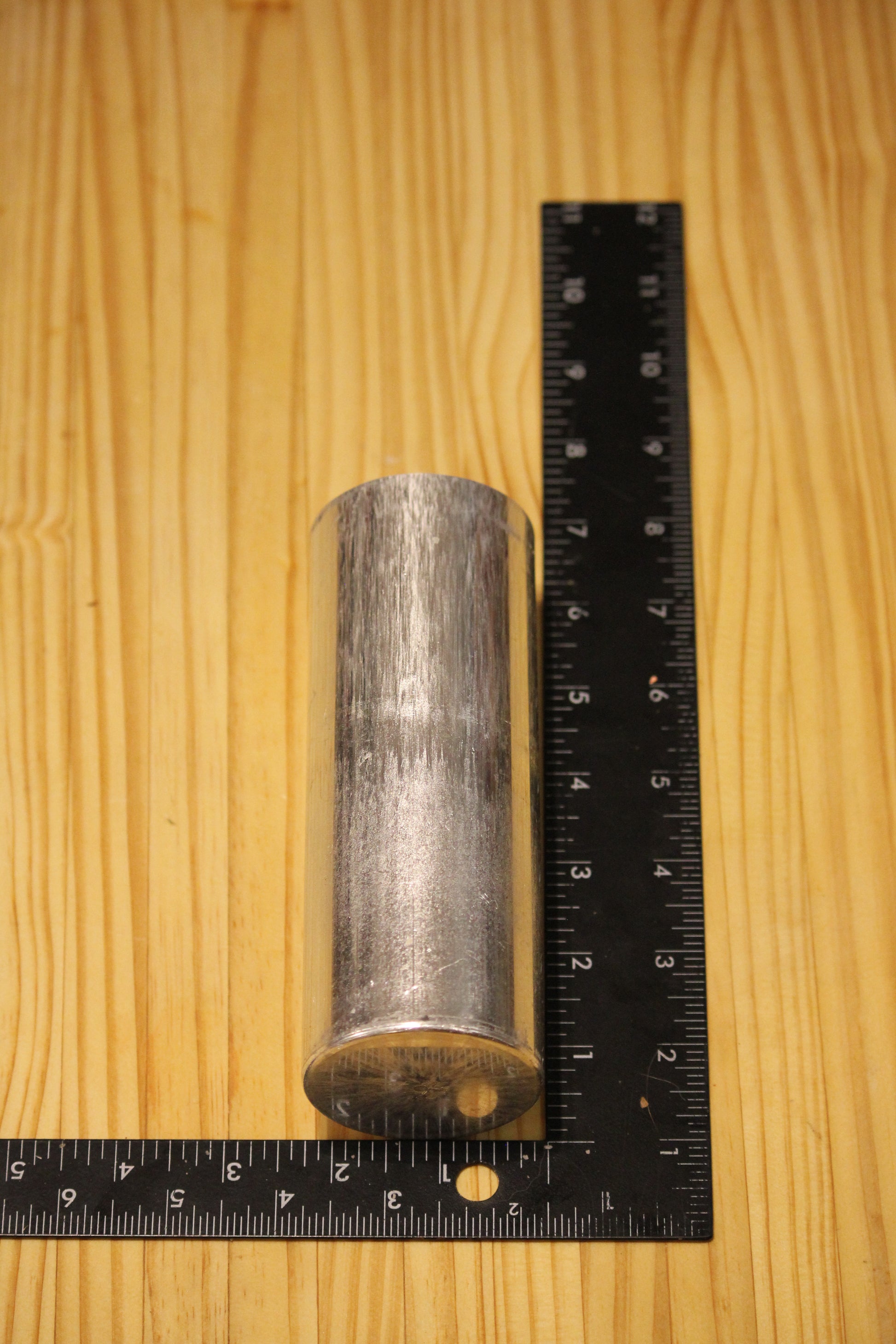 A cylindrical metal pillar mold, shown next to black rulers on a light wood grain background to indicate its dimensions.
