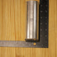 A small cylindrical metal pillar mold, shown on a light wood grain surface with a black ruler for scale.