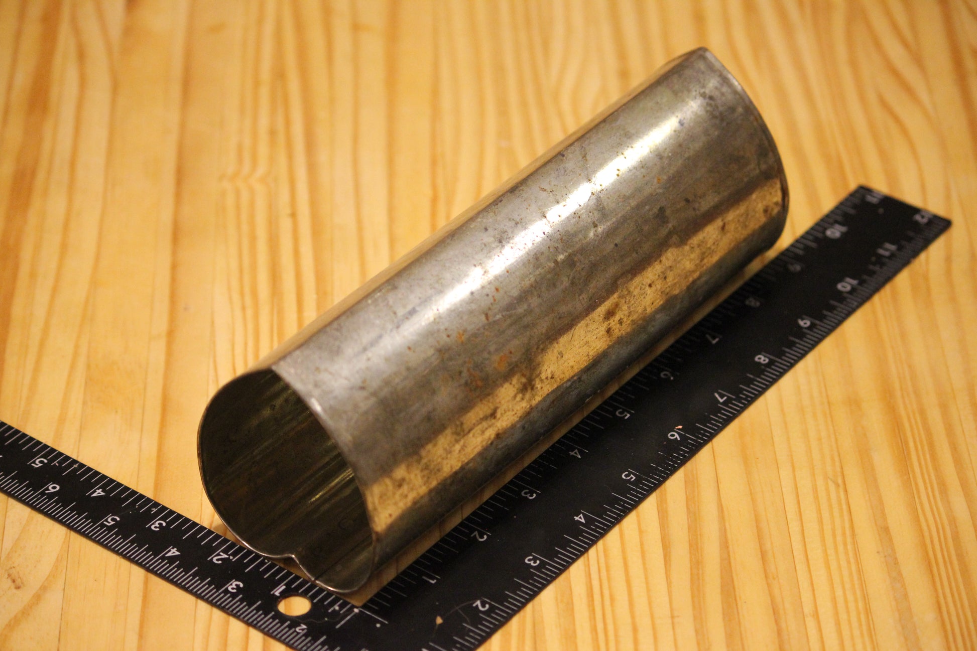 A metal heart shaped pillar mold, shown on a light wood grain background with a black ruler for scale.