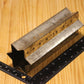 A metal star shaped pillar mold, shown on a light wood grain background with a black ruler for scale.