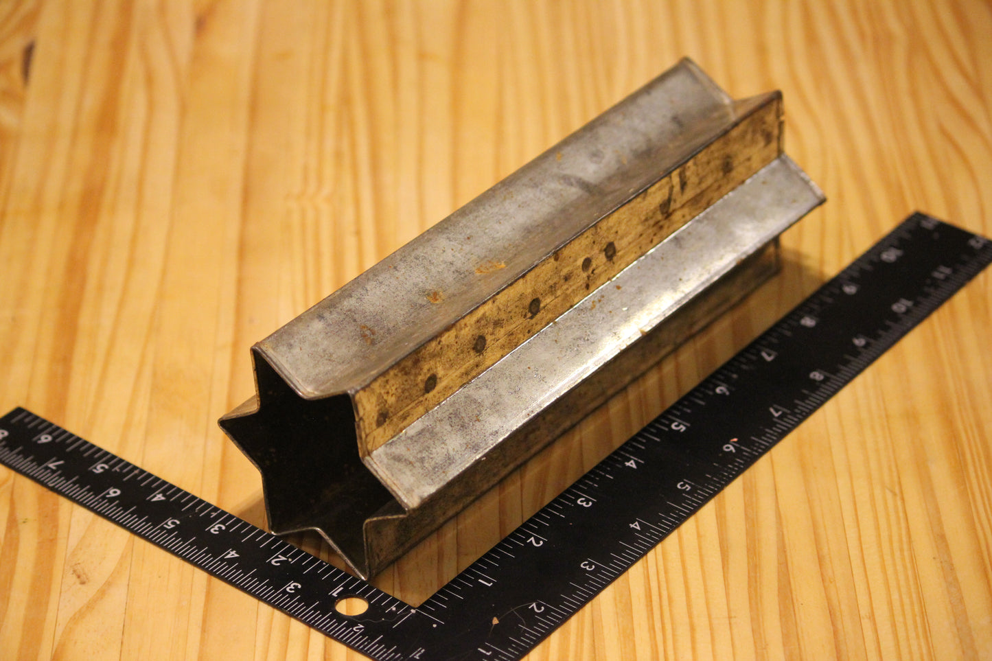 A metal star shaped pillar mold, shown on a light wood grain background with a black ruler for scale.