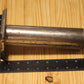 A metal cylindrical pillar mold, shown on a light wood grain background with a black ruler for scale.